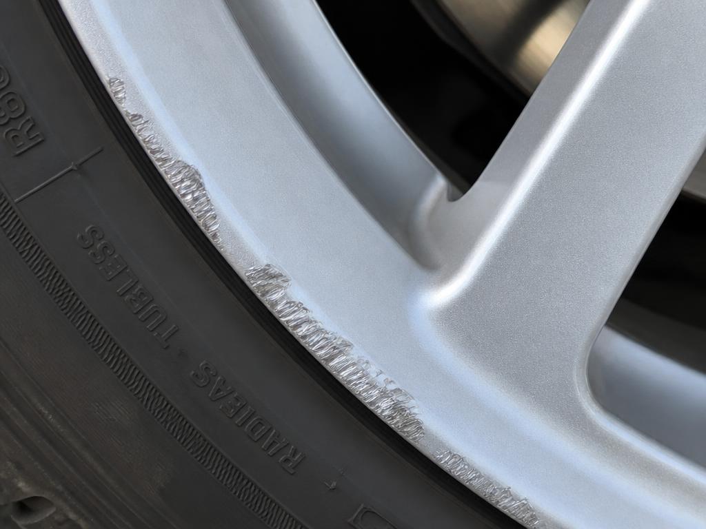 Kerb rash and paint loss scraped along the rim of a silver alloy wheel